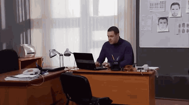 a man sits at a desk with a laptop and a pen in his hand