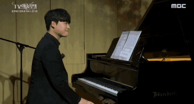 a man is playing a piano in front of a microphone with the letters mbc on the bottom