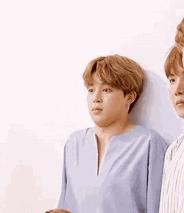 two young men are standing next to each other against a white wall . one of the men is wearing a blue shirt .