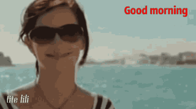 a woman wearing sunglasses is smiling in front of the ocean and the words good morning