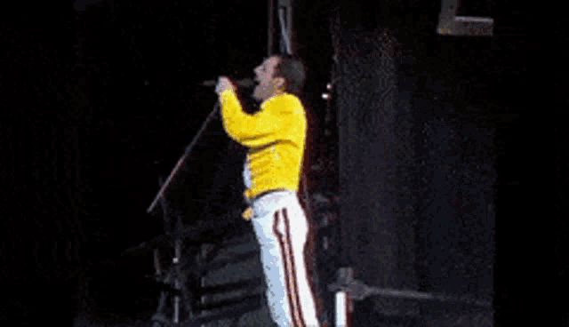a man in a yellow jacket is singing into a microphone on stage