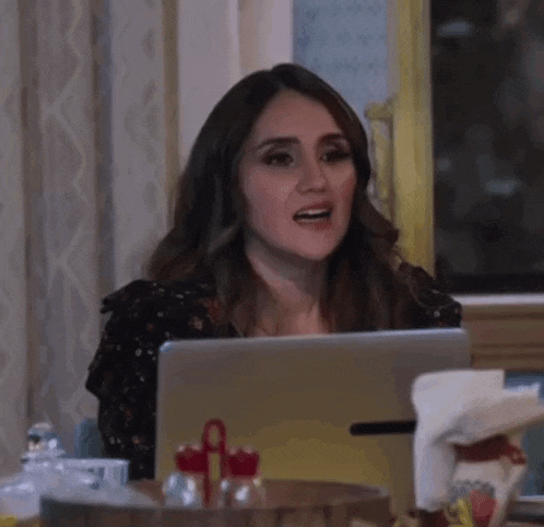 a woman is sitting at a table with a laptop computer and making a funny face .