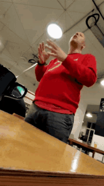 a man in a red sweater is sitting at a table with his hands in the air