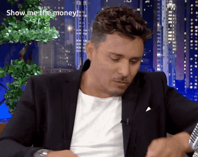 a man in a suit is looking at his watch and the words show me the money are behind him
