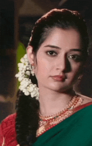 a woman with flowers in her hair is wearing a green saree and red top