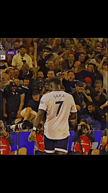 a soccer player with saka on the back of his jersey stands in front of a crowd