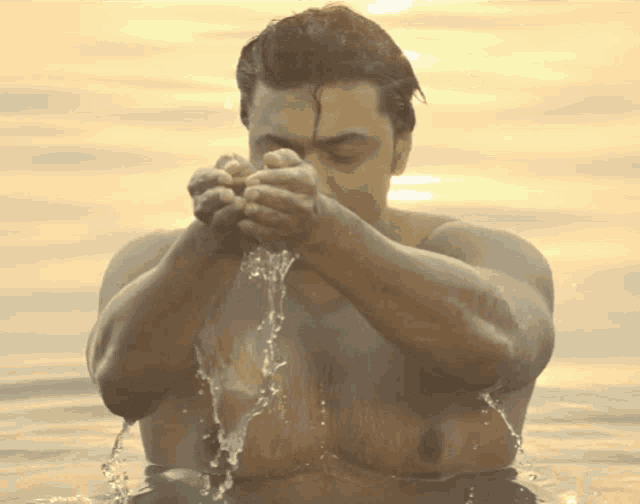 a shirtless man is standing in the water with his hands in his face