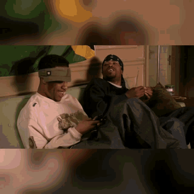 two men are sitting on a couch and one is wearing a headband that has the letter r on it