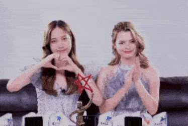 two women are making a heart shape with their hands while sitting on a couch