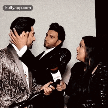 a man in a suit is hugging another man in a suit while a woman holds a camera .