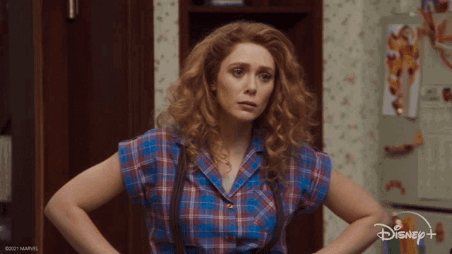 a woman in a plaid shirt is standing in front of a disney + sign