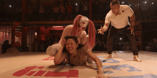 a woman in a pink mask holds another woman in a wrestling ring with the word gil on the floor