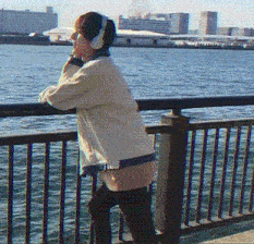 a woman wearing headphones leans against a railing overlooking the water