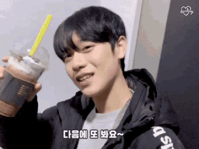 a young man is holding a cup of coffee with a yellow straw and smiling .