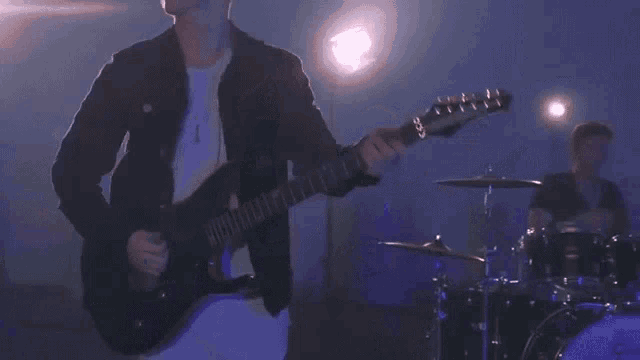 a man is playing a guitar and a drummer is playing drums on a stage .