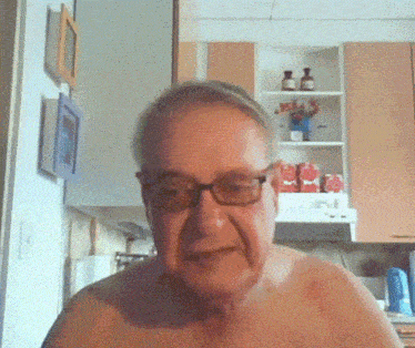 a shirtless man wearing glasses is standing in a kitchen