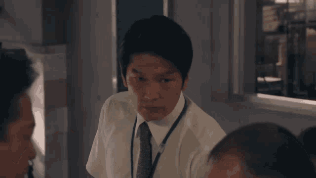 a man in a white shirt and tie with a lanyard around his neck looks at the camera