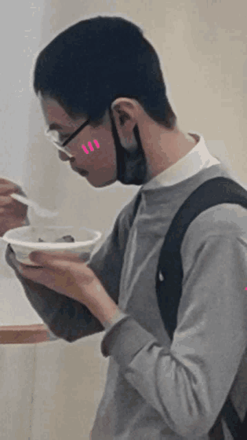 a young man wearing glasses and a mask is eating a bowl of food