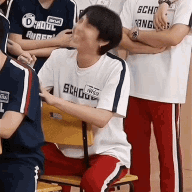 a man wearing a shirt that says scho on it is sitting in a chair