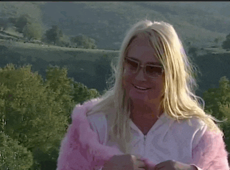 a blonde woman wearing sunglasses and a pink fur coat is smiling