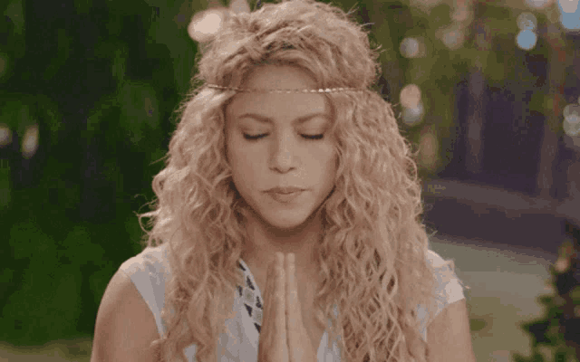 a woman with curly hair is praying with her eyes closed and her hands folded