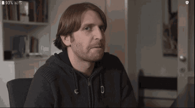 a man with a beard is wearing a black hoodie with the letter u on the front