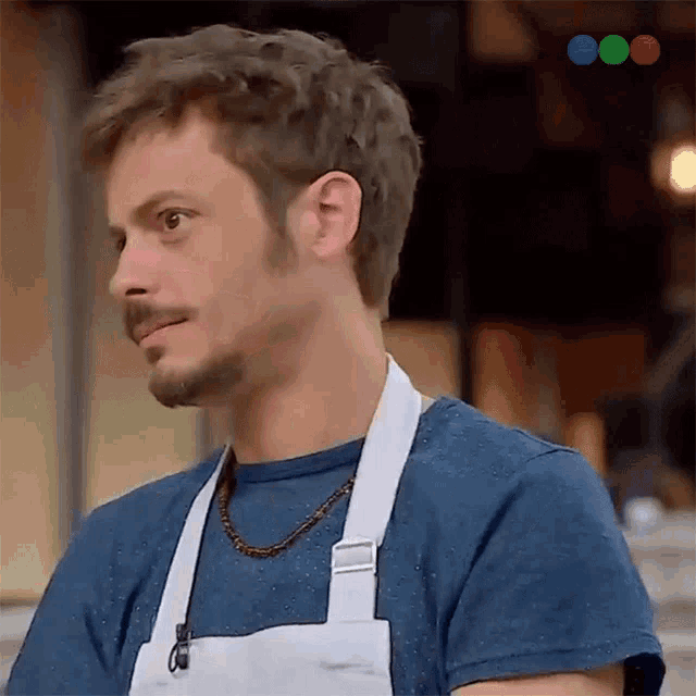 a man wearing an apron and a blue shirt is looking to the side