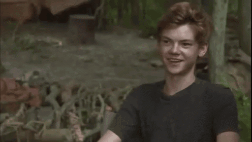 a young man in a black shirt is sitting in the woods .