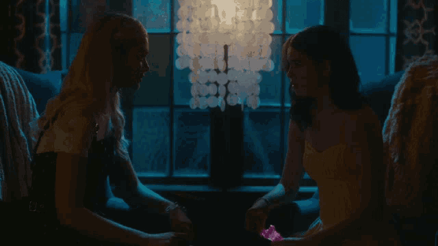 two women are sitting in front of a window holding hands