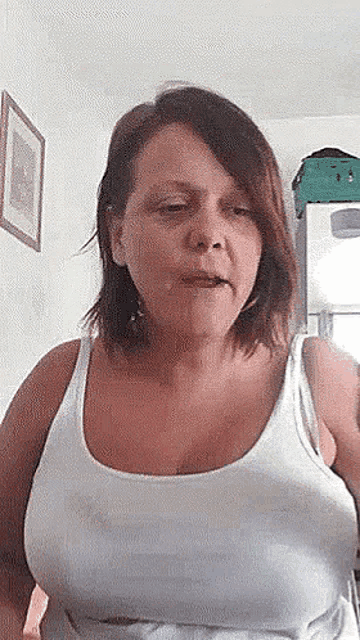a woman in a white tank top is making a funny face while standing in a room .