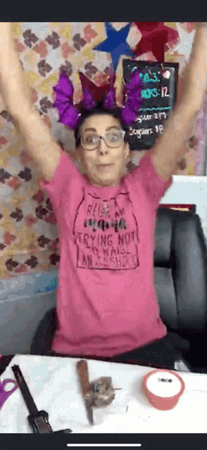 a woman in a pink shirt is sitting at a table with her arms in the air