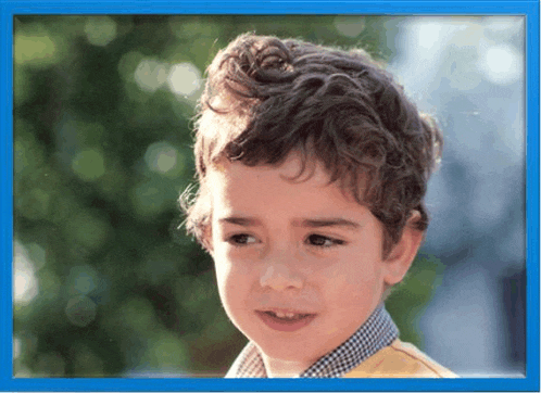 a young boy with curly hair is looking at the camera in a blue frame