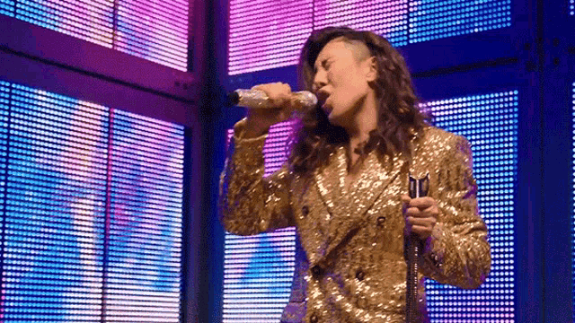 a woman in a sequined jacket is singing into a microphone .