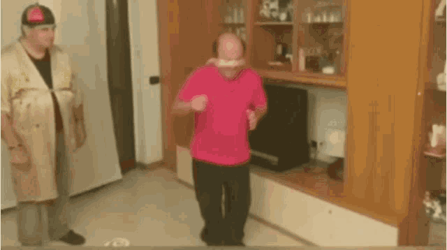 a man in a pink shirt is dancing with another man in a tan coat