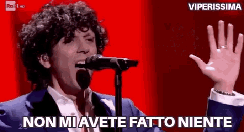 a man singing into a microphone with the words non mi avete fatto niente behind him .