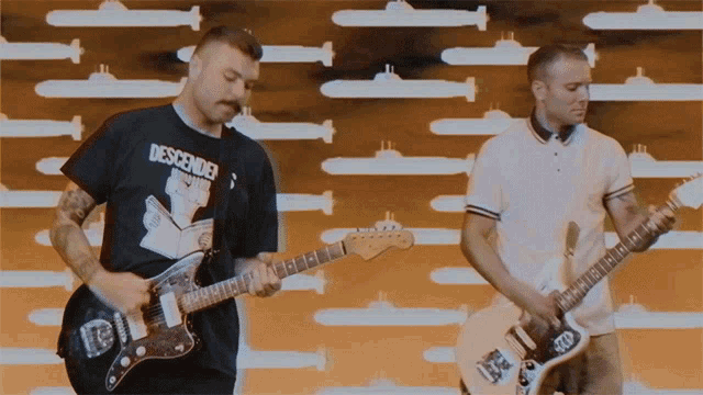 two men playing guitars with one wearing a shirt that says descender on it