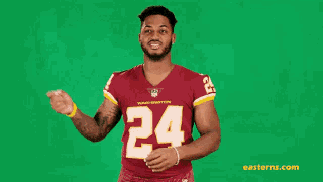 a man wearing a red jersey with the number 24 on it is standing in front of a green screen .