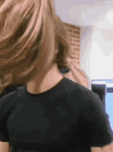 a woman in a black t-shirt is standing in front of a brick wall