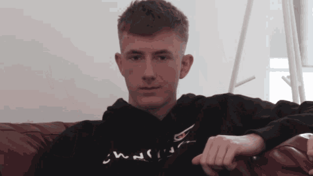 a young man is sitting on a couch wearing a black hoodie that says ' n ' on it
