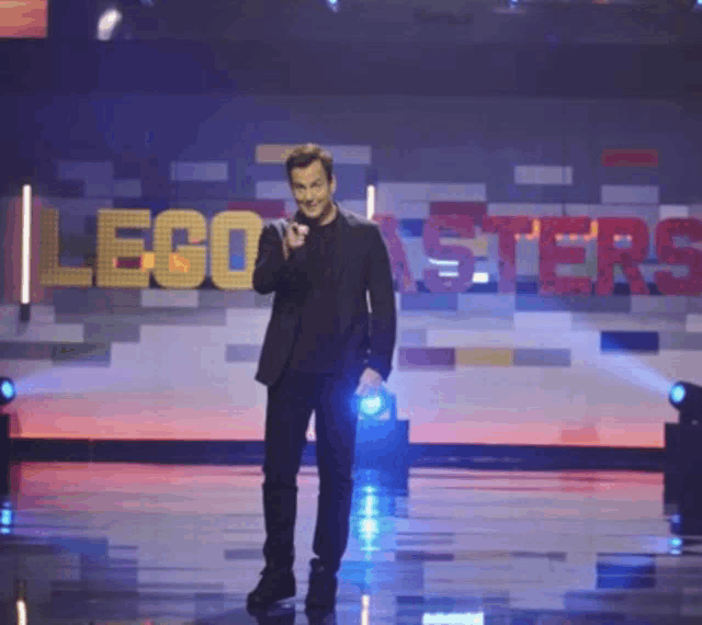 a man in a suit stands on a stage in front of a sign that says lego masters
