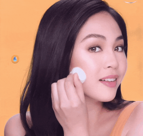 a woman wipes her face with a white cotton pad