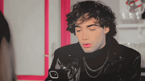 a young man with curly hair wearing a black turtleneck and a black leather jacket