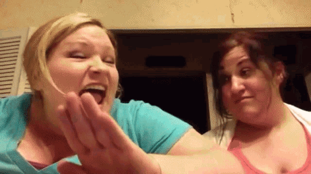 a woman in a blue shirt is making a funny face while another woman looks on
