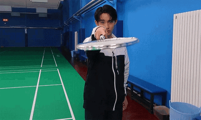 a man is holding a badminton racket on a court with a digital clock on the wall