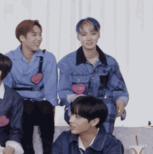 a group of young men are sitting on a couch with one wearing a denim jacket with a heart on it