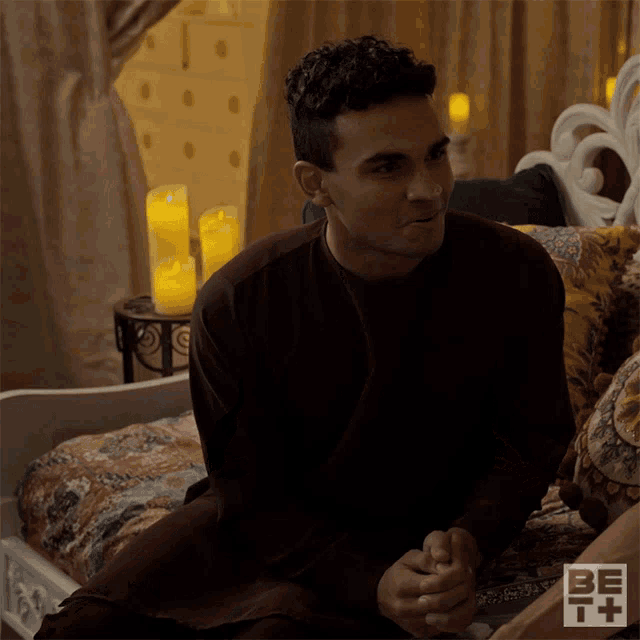 a man sits on a bed with candles in the background and a bet logo on the bottom right
