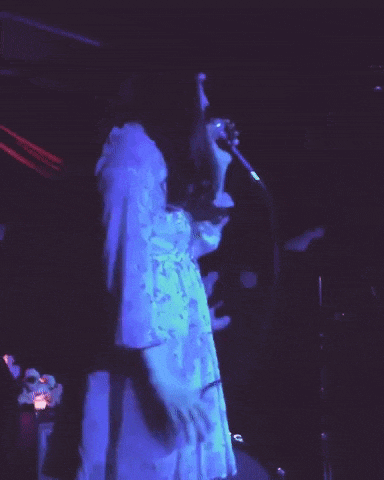 a woman in a white dress sings into a microphone in a dark room