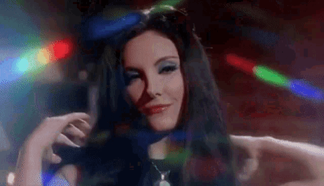 a woman with long black hair is standing in front of a disco ball in a dark room .
