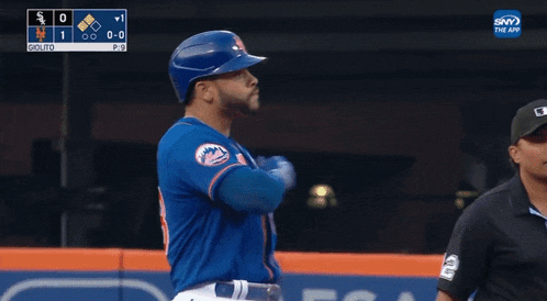a baseball player wearing a blue mets jersey is standing in front of a scoreboard