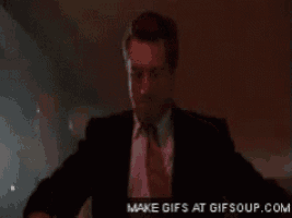 a man in a suit and tie is standing in a dark room with make gifs at gifsoup.com on the bottom right